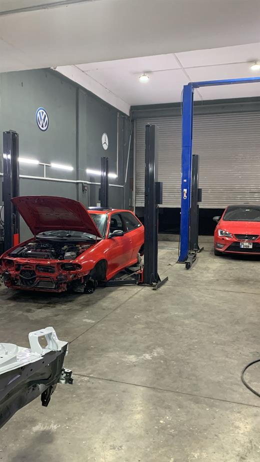 Kırmızı Opel Astra F GSi, garajda lift alanında kaputu açık ve ön takımı sökülmüş